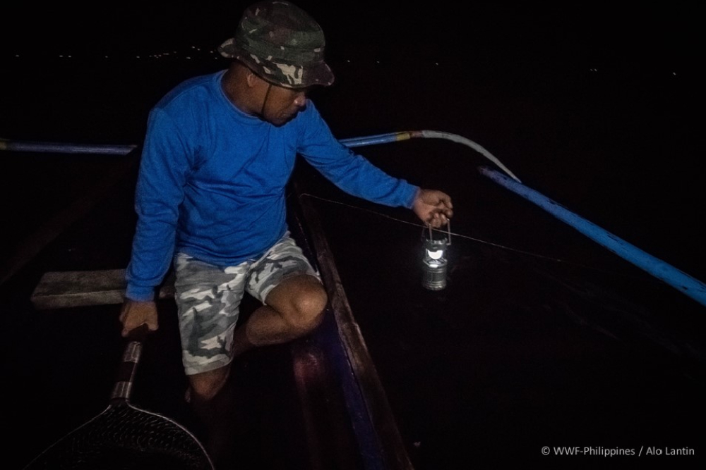 lagonoy gulf tuna fisherman joel bongkingki holds a solar lamp out over the sea as he waits for a catch to show