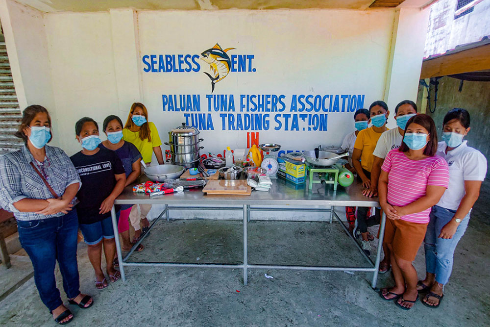 women from the paluan tuna fishers association stand next to the food processing equipment