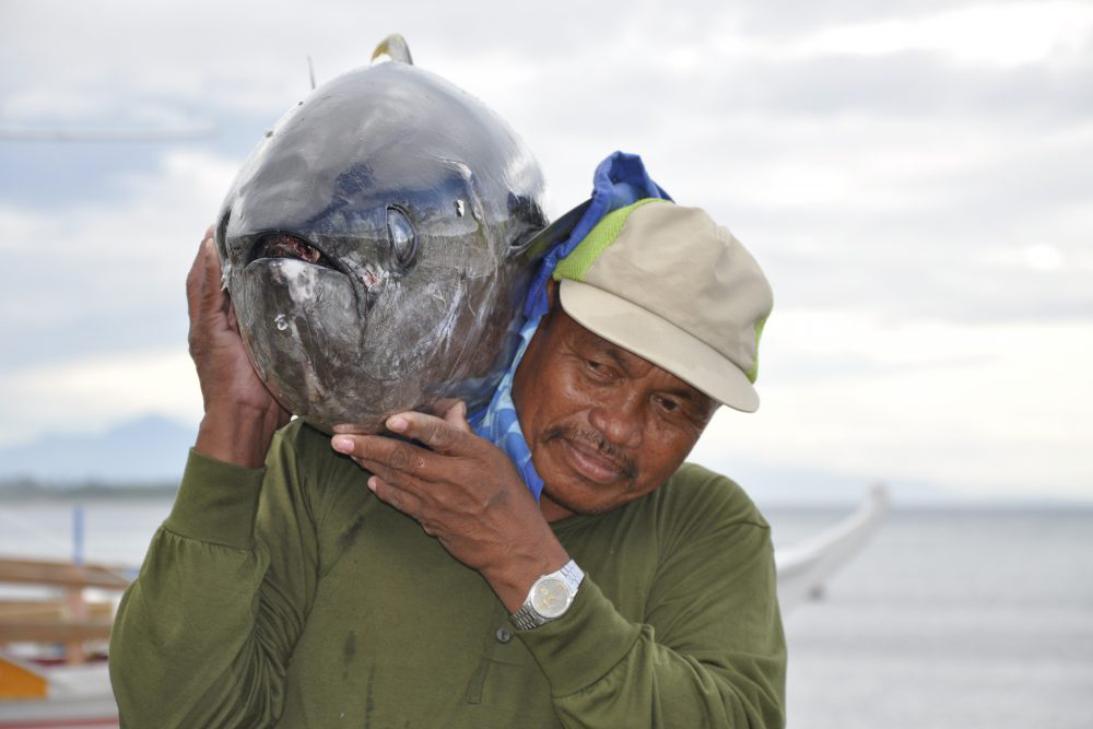 a fisherman carries a tuna to shore over his shoulder