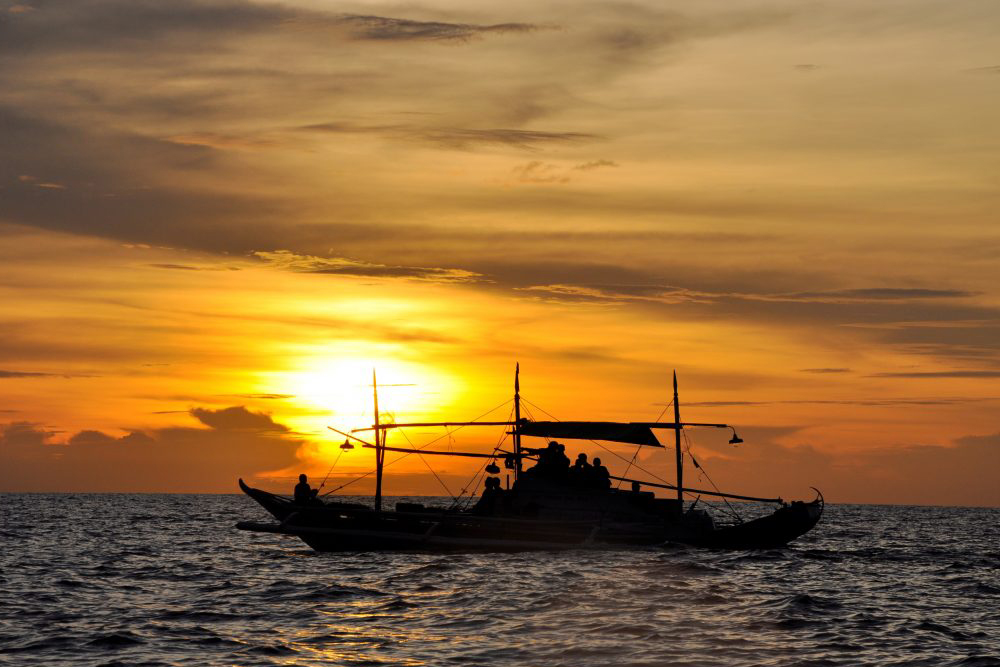 a fishing vessel sails against the sunset in mamburao mindoro