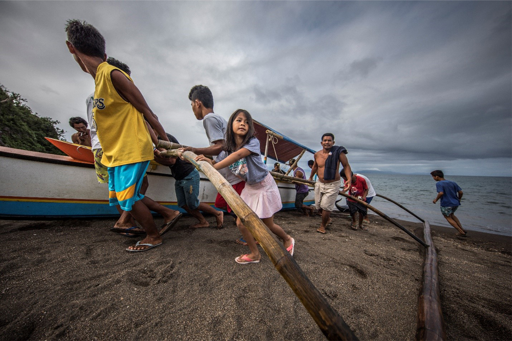 a young girl helps the people of her village haul a fishing boat back to shore off the coast of tabaco city philippines