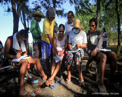 community members discuss their gslcs on a beach in tiwi albay under the shade of surrounding trees